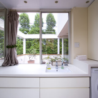 リビング上部は吹き抜けで、3階の部屋の気配も感じられる。テラスとリビングは同じ床材を使用し、アウトドアリビングのような連続性を感じられる開放的な空間だ。一方でダイニングは天井が低く、落ち着く場所となっている。北側の隣家の緑も借景として活用した
撮影：NewHouse出版