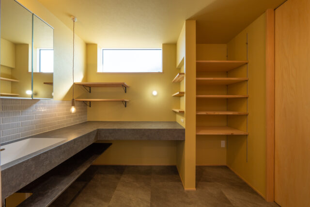 2階洗面室には大きな洗面カウンターを造作。内装は磁器質タイルや石目調のフロアタイルをセンス良く取り入れ、人に見せたくなるような空間に仕上げている。写真右の棚はタオルや部屋着の収納に最適。この洗面室はランドリールームとつながっていて、洗濯後はすぐにしまえる