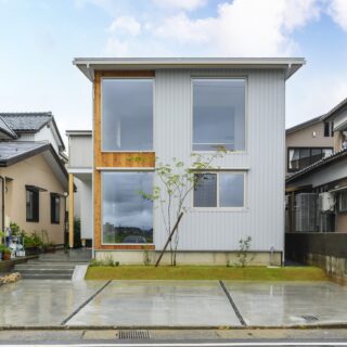 外観。建物はすっきりしたフォルム。そこに大胆に開口が設けられており、住宅というより店舗のような印象を受ける。箱のイメージで外観を仕上げるため、玄関は正面でなく左側面に設けた。共用部は木材、プライベート空間はガルバリウム鋼板と外壁を張り分け、アクセントとした。