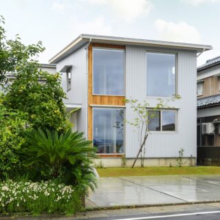 外観。車通りは多いが、駐車場があり道路から距離があることや、LDKを２階に上げたのに加え、壁の配置などによって外からの視線を気にすることなく暮らすことを叶えた。１階左側の窓は、店舗として使用する可能性がある玄関土間の様子をあえて見えるようにした。