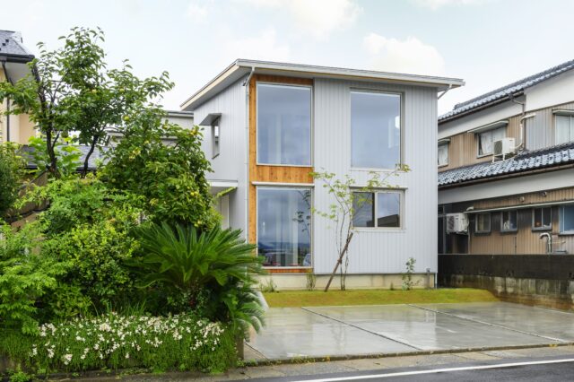 外観。車通りは多いが、駐車場があり道路から距離があることや、LDKを２階に上げたのに加え、壁の配置などによって外からの視線を気にすることなく暮らすことを叶えた。１階左側の窓は、店舗として使用する可能性がある玄関土間の様子をあえて見えるようにした。
