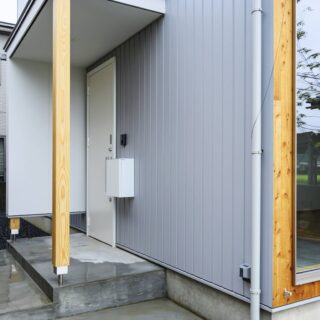 玄関ポーチ。柱を一番下まで落とすのではなく、袖壁や柱の下部に空きをつくり浮遊感を演出。住宅らしさを軽減した。画像右、木壁下部にある金具はアウターシェードを留めるもの。室内側からの視線の抜けは確保しながら日射を遮ることができる。日射遮蔽により冷房負荷の低減と冷房の効きやすさにもつながっている。