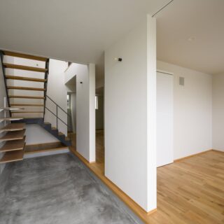 1階、玄関土間（左）右手前の個室は寝室。奥にファミリークローゼットやトイレ、２つの個室がある。玄関土間は、いつか古着店を開きたいという要望から計画された。造作の棚を設け、ディスプレイが楽しめる。寝室は店舗の接客室として使用する可能性もあるため、戸を省いた。