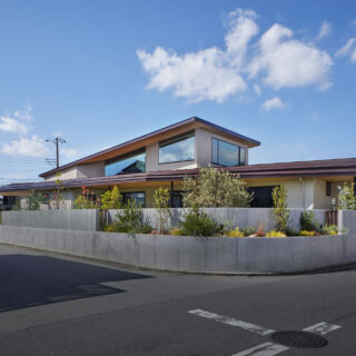 南から見た外観。プライバシーを守るための外構は、一部の植栽は道路に向けて開き威圧感を軽減。コンクリートはリブ付きとし、柔らかさをプラスした。まっすぐに伸びる１階の屋根と、捲り上がるような２階の屋根。どちらも伸びやかで、家に大らかさが感じられる