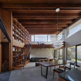 キッチンからダイニング、一段下がったリビング、2階のロフトを見渡す。画像右が南に続くデッキから庭と、画像左の暖炉テラスが建物のラインに対して斜めに交わるため、より強く空間の広がりを実感できる。画像右奥の通路の奥にラウンジとシアタールームを設けた