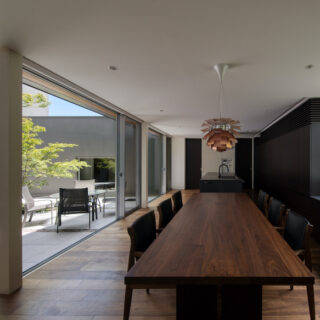 来客の多いライフスタイルに合わせ、ロングサイズのテーブルやパーティー用シンクを備えた機能的な空間に。背面の造作棚には、家電やゴミ箱、さらには神棚までもが美しく収まり、生活感を鮮やかに消し去っている。