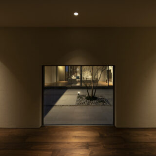 玄関に足を踏み入れると、そこには中庭を囲む回廊が広がっている。正面の壁に設けられた低めの開口からは、中庭の緑とその先に広がるリビングが顔をのぞかせる。あえて視線を絞ることで、その先にある開放感への好奇心を誘う