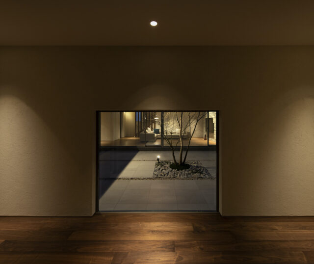 玄関に足を踏み入れると、そこには中庭を囲む回廊が広がっている。正面の壁に設けられた低めの開口からは、中庭の緑とその先に広がるリビングが顔をのぞかせる。あえて視線を絞ることで、その先にある開放感への好奇心を誘う