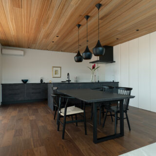 ダイニング・キッチン。リビングと対象的な、落ち着きを感じられる暗めの配色で落ち着ける空間に。冷蔵庫などのキッチン家電は、右奥のパントリーに集約されている。ピクチャーレールやダウンライト、キッチンと同じ高さの造作収納はアートスペース。キッチン背後を、生活感のないアートスペースにという田井さんの提案だ