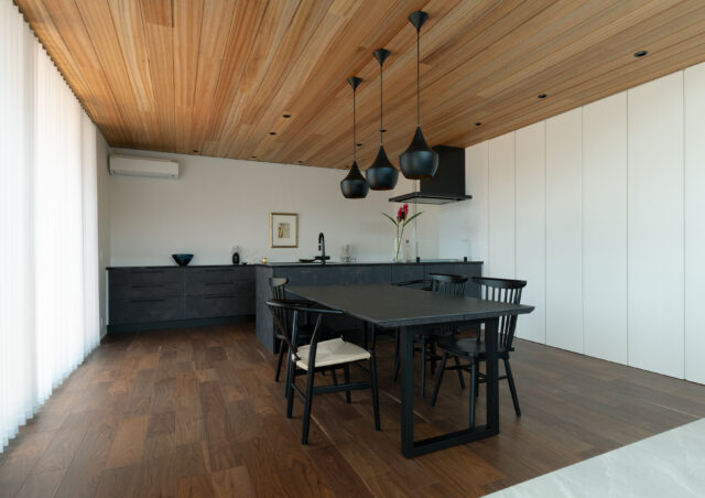 ダイニング・キッチン。リビングと対象的な、落ち着きを感じられる暗めの配色で落ち着ける空間に。冷蔵庫などのキッチン家電は、右奥のパントリーに集約されている。ピクチャーレールやダウンライト、キッチンと同じ高さの造作収納はアートスペース。キッチン背後を、生活感のないアートスペースにという田井さんの提案だ