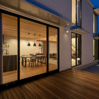 ウッドデッキ夕景。専用の照明も設置済みだ。それぞれの窓の上部に日差し調整のための庇があることがわかる。ダイニングを使う時間が長いので、ウッドデッキはこの位置に。アウトドアダイニングのような使い方ができる