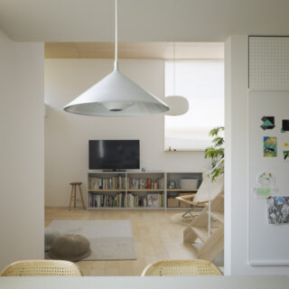 ダイニングからリビングを見る。天井高や素材の違い、袖壁のおかげで建具がなくとも空間の切り替わりが明確に。画像右のマグネットボードやルーター置き場はデザイン性と実用性を確保。リビングからの死角となる袖壁裏に配置し生活感があふれがちなスペースが目立たないようにした