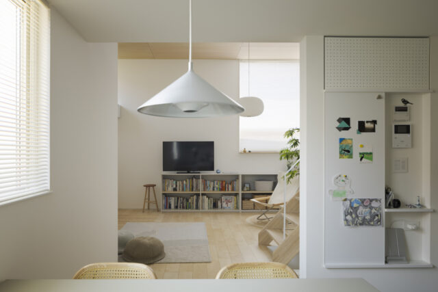 ダイニングからリビングを見る。天井高や素材の違い、袖壁のおかげで建具がなくとも空間の切り替わりが明確に。画像右のマグネットボードやルーター置き場はデザイン性と実用性を確保。リビングからの死角となる袖壁裏に配置し生活感があふれがちなスペースが目立たないようにした