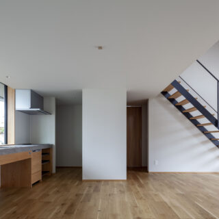 陽光が入る明るいキッチン・ダイニング。キッチンは幹線道路に面した北側に窓があるが、北の庭と植栽・木塀によってプライバシーを守り、粉塵や排気ガスも遠ざけている。写真正面奥の白い壁の両サイドは造作収納。キッチン側は調理家電などを見えないようにしまっておける