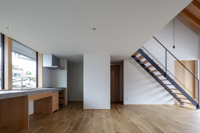 陽光が入る明るいキッチン・ダイニング。キッチンは幹線道路に面した北側に窓があるが、北の庭と植栽・木塀によってプライバシーを守り、粉塵や排気ガスも遠ざけている。写真正面奥の白い壁の両サイドは造作収納。キッチン側は調理家電などを見えないようにしまっておける