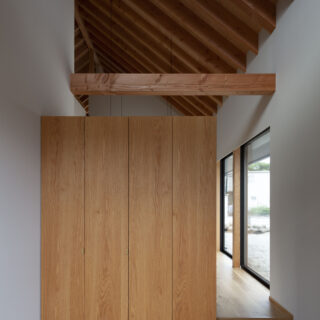 玄関土間。正面は大型収納で仕切っているが上部はつながっていて、整然と並ぶ垂木が奥行きを感じさせる