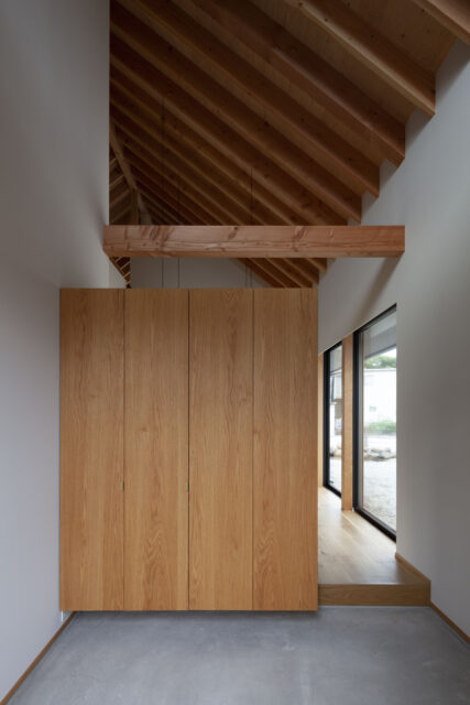 玄関土間。正面は大型収納で仕切っているが上部はつながっていて、整然と並ぶ垂木が奥行きを感じさせる