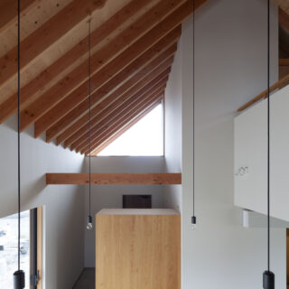 階段からLDKを見る。おおらかな天井を支える無数の垂木は、玄関上部の窓を介して屋外まで続く
