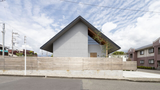 切妻の大きな三角屋根が印象的なファサード。奥村さんは大屋根で家の南北を覆い、かつ、南北2つの庭もつくって周辺環境の影響を軽減。北（写真左）の庭は幹線道路の排気ガスや粉塵を遠ざける役割、南（写真右）の庭は庭づくりを楽しみ集合住宅の目線を遮る役割を果たす
