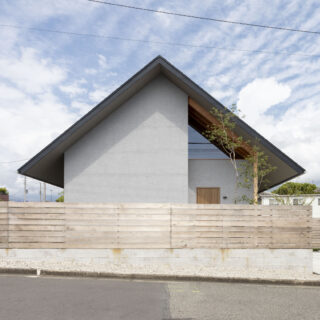 切妻の大きな三角屋根が印象的なファサード。奥村さんは大屋根で家の南北を覆い、かつ、南北2つの庭もつくって周辺環境の影響を軽減。北（写真左）の庭は幹線道路の排気ガスや粉塵を遠ざける役割、南（写真右）の庭は庭づくりを楽しみ集合住宅の目線を遮る役割を果たす
