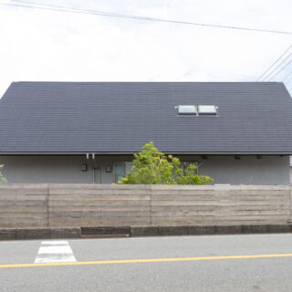 敷地の北を走る幹線道路から見た「サンカクヤネノイエ」。車の騒音や排気ガスから生活空間を守るために大屋根と木塀で覆い、1階の窓部分は植栽で目隠ししている。2階はほとんど窓がなく全体的に閉じた印象だが、邸内にはこの外観から想像もつかない明るい大空間が広がる