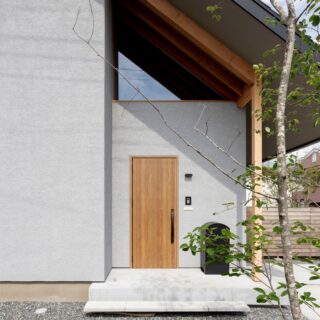 玄関。木製ドアや軒の垂木が温かみを醸す。三角窓からは内部の垂木が垣間見え、のびやかな空間を想像させる