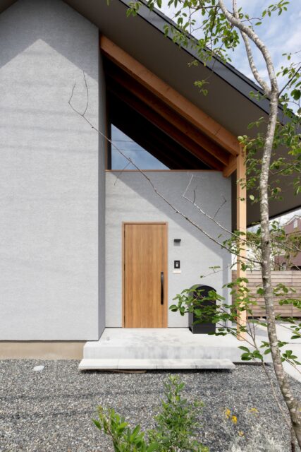 玄関。木製ドアや軒の垂木が温かみを醸す。三角窓からは内部の垂木が垣間見え、のびやかな空間を想像させる