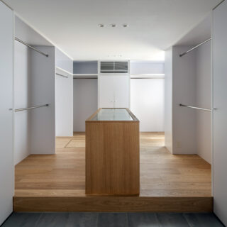 手前にシューズクローク、靴を脱いで上がった場所に造作のアクセサリーケースとハンガー収納を設えた多機能な衣装部屋。ガラスケースの下は引き出し収納になっている