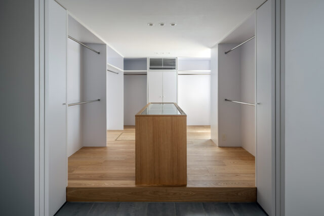 手前にシューズクローク、靴を脱いで上がった場所に造作のアクセサリーケースとハンガー収納を設えた多機能な衣装部屋。ガラスケースの下は引き出し収納になっている
