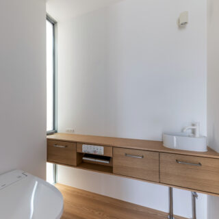 来客用の2階トイレ。手洗い・ペーパーホルダー・収納の機能を集約した造作カウンターは、窓に突き刺さるようなデザインとすることで空間の広がりと奥行を強調している