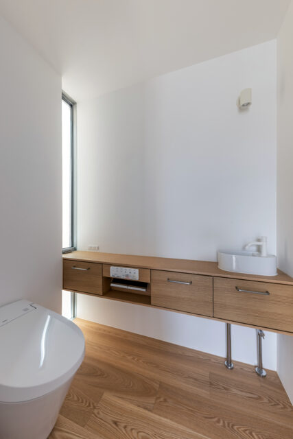 来客用の2階トイレ。手洗い・ペーパーホルダー・収納の機能を集約した造作カウンターは、窓に突き刺さるようなデザインとすることで空間の広がりと奥行を強調している