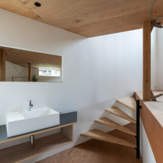 トイレの隣にある洗面コーナー。鏡は実用性と共に、空間を反射し広がりを感じさせる役割も。壁に沿って回り込むような螺旋階段でリビングへと進む。