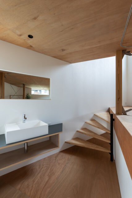 トイレの隣にある洗面コーナー。鏡は実用性と共に、空間を反射し広がりを感じさせる役割も。壁に沿って回り込むような螺旋階段でリビングへと進む。