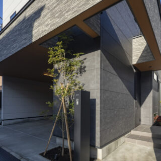 外観。画像右は玄関ポーチ、奥にお母さまが植栽を楽しむ坪庭がある。左のガレージからも直接室内に入れるよう計画した。ガレージ脇、玄関扉から手前はシューズインクローゼット。収納力は抜群で、2世帯分の納戸としても使われている